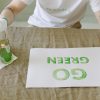 Personne peignant un message éco-responsable 'Allez Vert' sur du papier avec des gants et un pinceau.