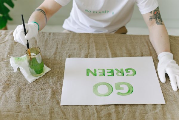 Personne peignant un message éco-responsable 'Allez Vert' sur du papier avec des gants et un pinceau.