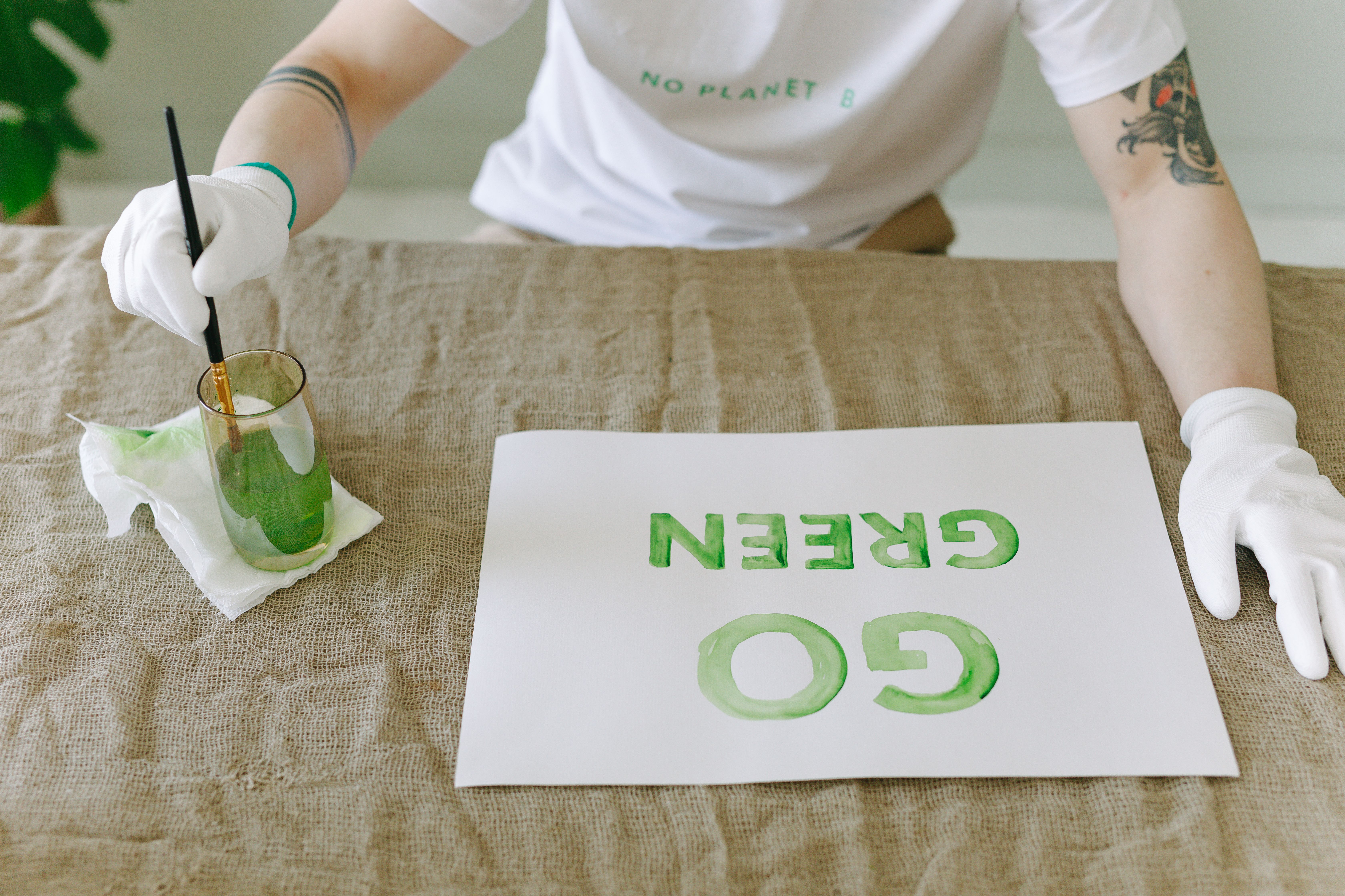 Personne peignant un message éco-responsable 'Allez Vert' sur du papier avec des gants et un pinceau.
